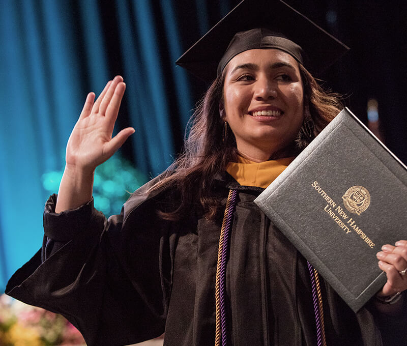 A proud SNHU student holding her diploma on the graduation stage